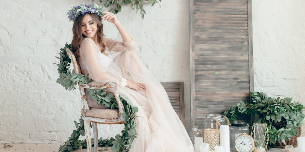 A girl in a beige peignoir, with a wreath of flowers on her head, poses in the studio loft, fine art wedding style