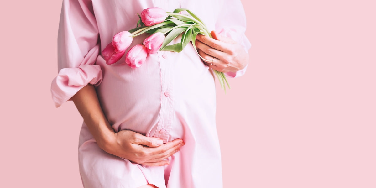 Pregnancy, motherhood, Mother's Day holiday concept. Young woman wearing maternity shirt dress with tulip flowers holding hands on belly. Beautiful pregnant woman is waiting for the birth of her baby