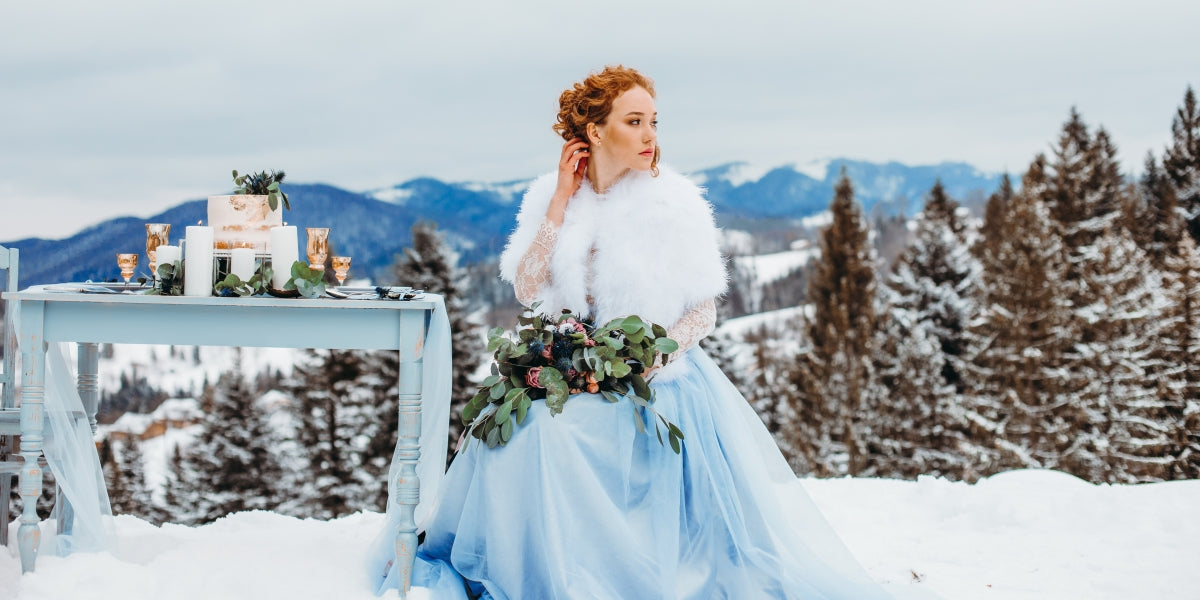 Elegant red-haired girl with a bouquet in her hands sitting on a chair against the backdrop of winter mountains