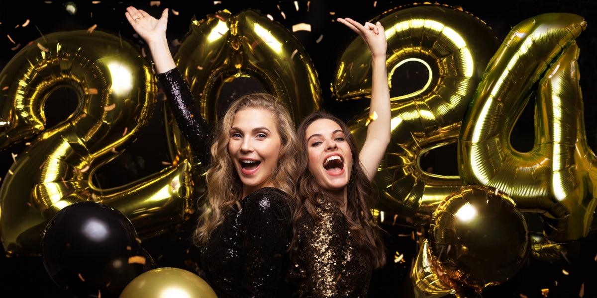 Happy gorgeous girls in stylish sexy party dresses holding gold 2024 balloons, having fun at New Year's Eve Party