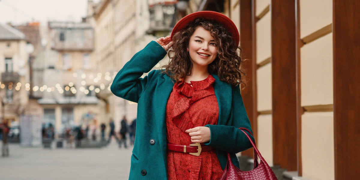 Happy smiling fashionable curvy woman wearing trendy autumn outfit orange hat, snakeskin print dress, belt, green coat, holding red wicker leather bag, posing in street of European city.