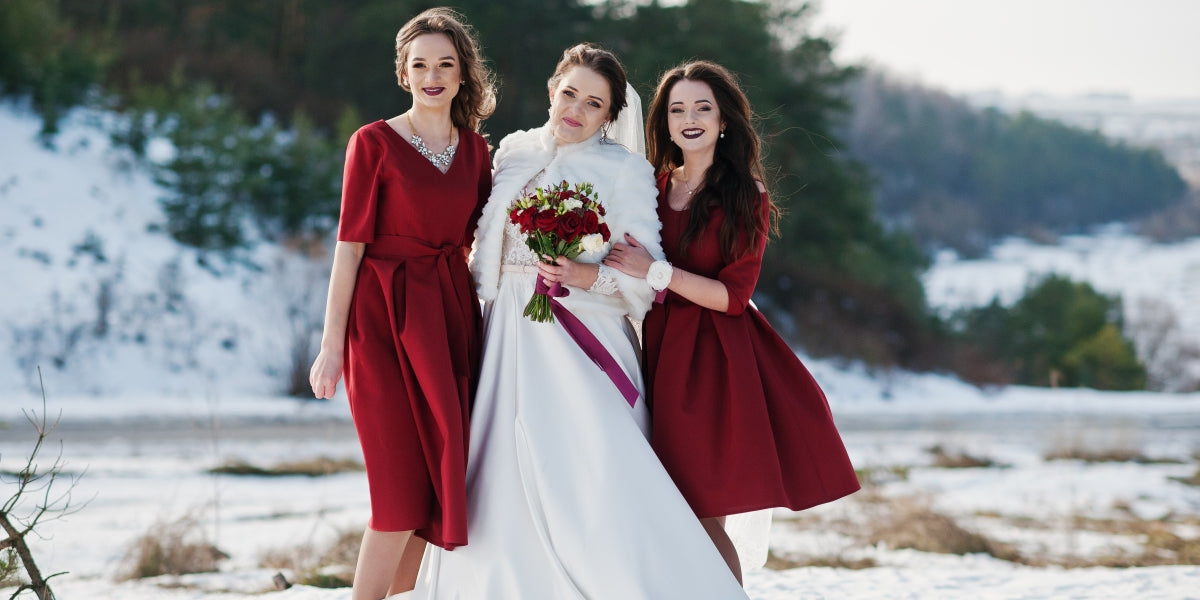 Pretty bridesmaids on red dresses with bride on sunny winter wedding day.